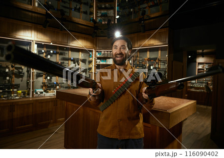 Crazy excited hunter weapon shop client laughing ominously standing with rifles Crazy excited hunter weapon shop client laughing ominously standing with rifles 116090402