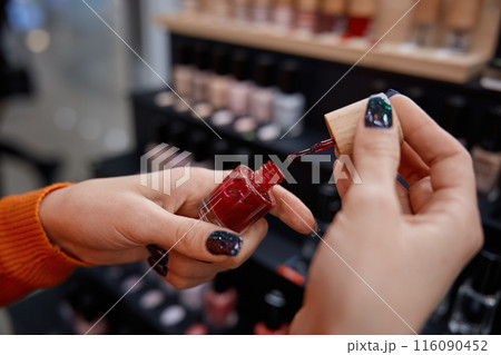 Woman hands holding bright red nail polish in cosmetics store Woman hands holding bright red nail polish in cosmetics store 116090452