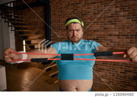 Funny chubby man in sportswear fooling around with fitness equipment 116090480