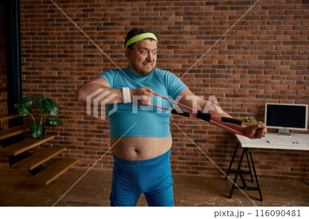 Comic chubby man in sportswear fooling around with fitness equipment 116090481