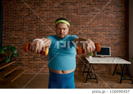 Portrait of serious comic man with obese figure doing workout with dumbbells 116090487