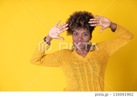 Young pretty smiling black woman showing palms with curly afro hair, wearing yellow sweater on yellow background, with copy space. Happiness concept. Young pretty smiling black woman showing palms with curly afro hair, wearing yellow sweater on yellow background, with copy space. Happiness concept. 116091902