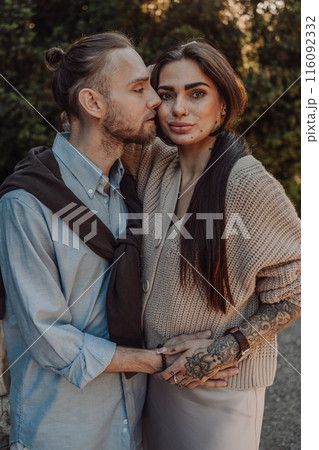 Smiling tattooed girl hugging her boyfriend in a park. Pretty redhead woman with tattoos and man on a walk. 116092332