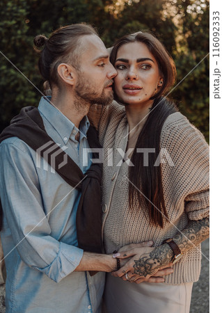 Smiling tattooed girl hugging her boyfriend in a park. Pretty redhead woman with tattoos and man on a walk. Smiling tattooed girl hugging her boyfriend in a park. Pretty redhead woman with tattoos and man on a walk. 116092333