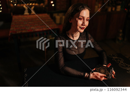 Closeup portrait of mysterious fortuneteller shuffling deck of tarot cards by light of burning candles. Enigmatic warlock performing esoteric rite, forecasting fate. Concept of divination, magic. 116092344