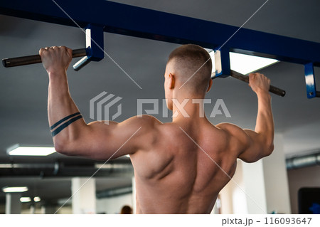 Bodybuilder performs a pull-up exercise at a gym, showcasing his muscular back Bodybuilder performs a pull-up exercise at a gym, showcasing his muscular back 116093647