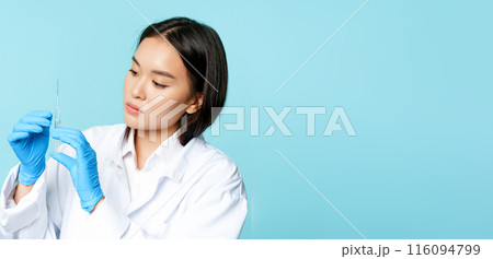 Image of asian female nurse, doctor in uniform and gloves, holding syringe, standing over blue background Image of asian female nurse, doctor in uniform and gloves, holding syringe, standing over blue background 116094799