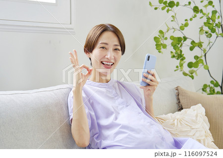 自宅でスマートフォンを持ってOKサインをする高廉妊娠をした妊婦 116097524