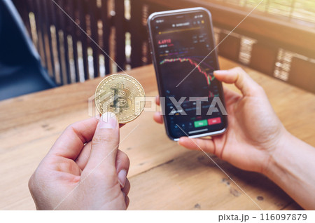 Someone checking Bitcoin price chart on digital exchange on smartphone while holding Bitcoin token. Someone checking Bitcoin price chart on digital exchange on smartphone while holding Bitcoin token. 116097879