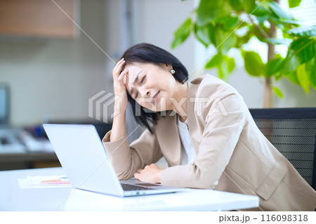 オフィスで頭を抱える渋い顔のミドル女性 オフィスで頭を抱える渋い顔のミドル女性 116098318