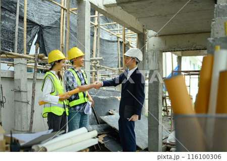 Handsome businessman in black suit and engineer shaking hands on construction site 116100306