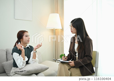 Young female patient sitting on sofa and telling about her problem to psychologist 116100404