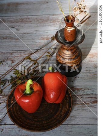 Red peppers on a clay plate, branches of wild rose and a wooden vase with dried flowers 116100656