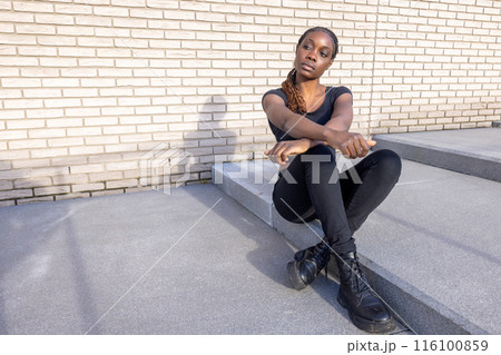 On city steps, a fashionable young lady in a trendy black outfit exudes confidence and style On city steps, a fashionable young lady in a trendy black outfit exudes confidence and style 116100859