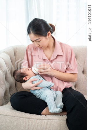 A caring Asian mom is holding her newborn baby son in her arm and feeding him milk from a bottle. 116101081