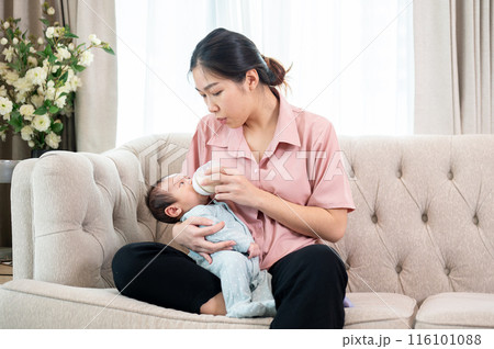 A caring Asian mom is holding her newborn baby son in her arm and feeding him milk from a bottle. A caring Asian mom is holding her newborn baby son in her arm and feeding him milk from a bottle. 116101088
