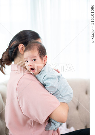 An Asian mom is cuddling her newborn baby while standing by the window indoors. motherhood 116101096