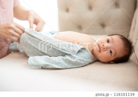 A caring mom is putting pajamas on her newborn baby son on a couch in the living room. 116101139