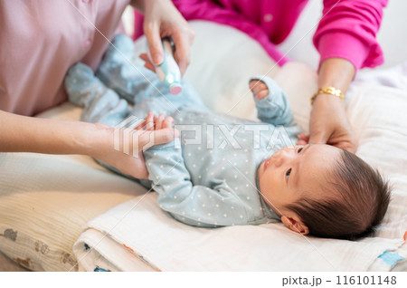 An infant baby boy is having his nails trimmed by an electronic baby nail trimmer held by his mom. An infant baby boy is having his nails trimmed by an electronic baby nail trimmer held by his mom. 116101148