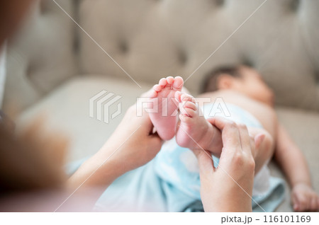 A close-up image of a mom lifting her newborn baby's legs up to change his diaper and put clothes on 116101169