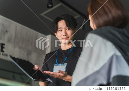 ジムで女性会員に運動メニューの説明・指導をするトレーナー・インストラクターの若いアジア人男性 ジムで女性会員に運動メニューの説明・指導をするトレーナー・インストラクターの若いアジア人男性 116101331