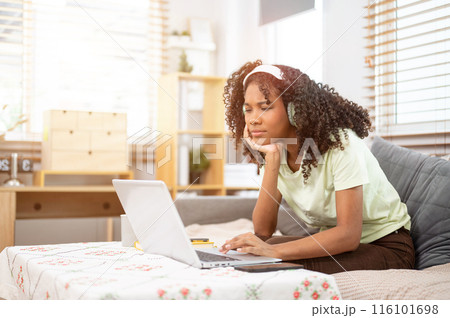 A perplexed young Black woman looks confused while reading an online blog or emails on her laptop. 116101698