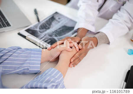 A close-up image of a caring female doctor holding a patient's hand to comfort and reassure them. 116101789
