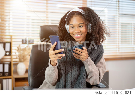 An attractive Black woman is scrolling on her phone while having morning coffee at a desk. An attractive Black woman is scrolling on her phone while having morning coffee at a desk. 116101821