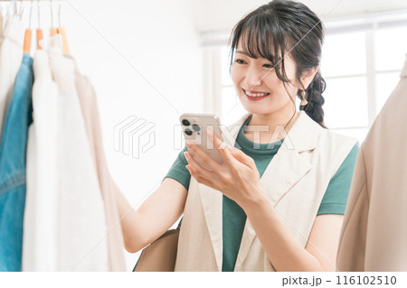 スマホを見ながらアパレルショップで買い物をする若いアジア人女性 116102510