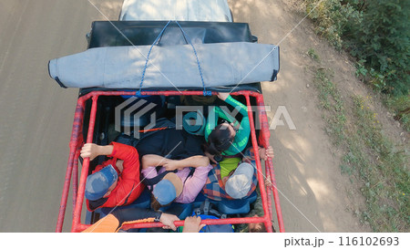 Adventure Journey in Utility Vehicle. Top view of a utility vehicle loaded with passengers and cargo, traveling on a dirt road, an outdoor excursion or adventure. 116102693