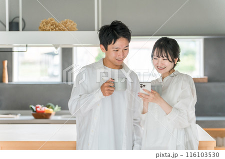 家のダイニングでコーヒーを飲みながらスマホを見る夫婦・カップル 116103530