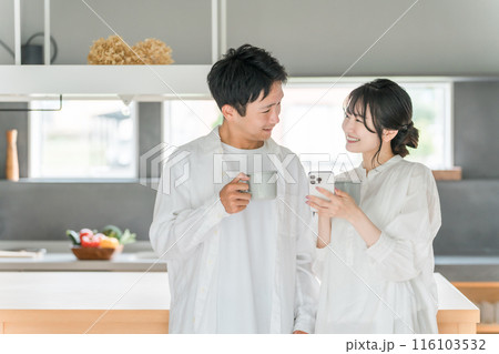 家のダイニングでコーヒーを飲みながらスマホを見る夫婦・カップル 116103532