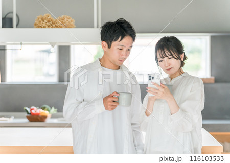 家のダイニングでコーヒーを飲みながらスマホを見る夫婦・カップル 家のダイニングでコーヒーを飲みながらスマホを見る夫婦・カップル 116103533