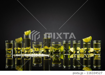 Tequila shots with lime slices and salt on a black reflective background. Tequila shots with lime slices and salt on a black reflective background. 116104527