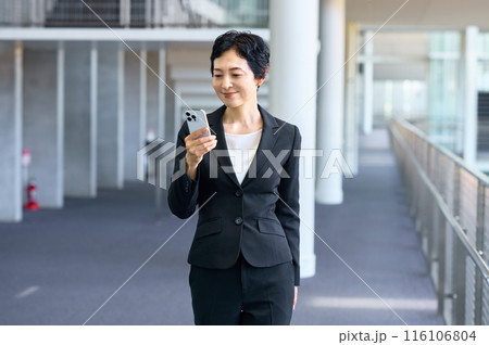 オフィスの廊下でスマホを持って立つスーツ姿のビジネスウーマン 116106804