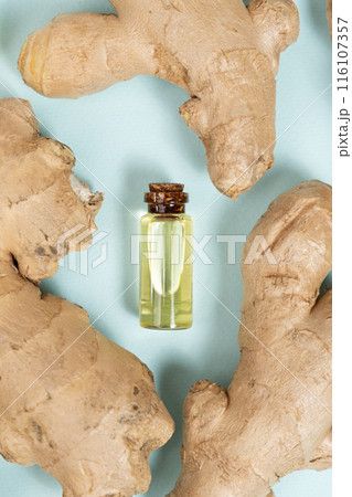 Natural ginger oil in glass bottle among ginger root top view. Natural ginger oil in glass bottle among ginger root top view. 116107357