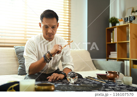 Male tarot reader making predictions at table surrounded by various spiritual items Male tarot reader making predictions at table surrounded by various spiritual items 116107570