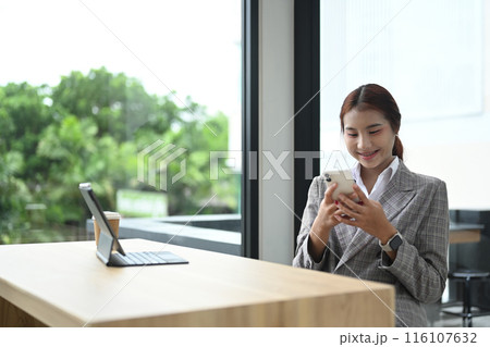 Attractive young businesswoman wearing suit using mobile phone at desk in the modern office Attractive young businesswoman wearing suit using mobile phone at desk in the modern office 116107632