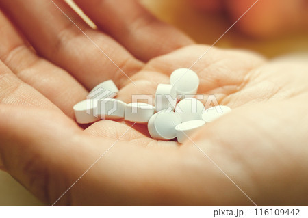 White round medical pills lie in hand, close up. These could be vitamins or antibiotics or pain relievers or any other. 116109442
