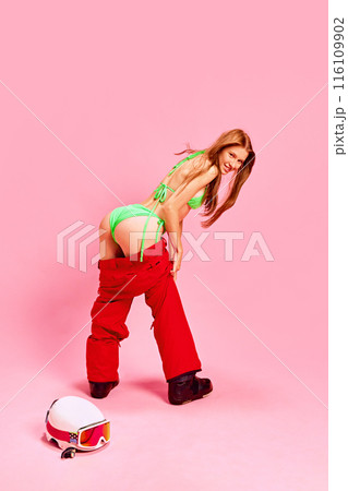 Woman combining summer and winter attire, showcasing her fit body with funny pose against pink studio background. Summer vs winter 116109902
