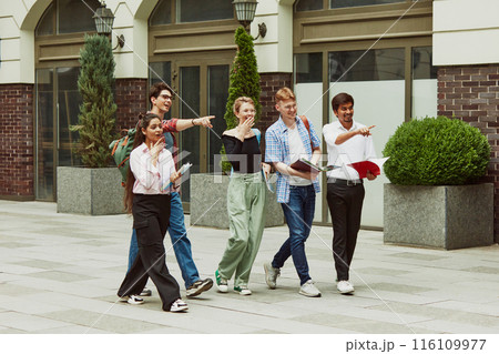 Group of multiracial people, boys and girls, students walking outside the university and pointing somewhere with excitement 116109977