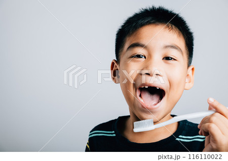 An adorable Asian boy missing an upper milk tooth holds a toothbrush showcasing dental care routine and the happiness of learning. Isolated on white background. Children dentist routine 116110022