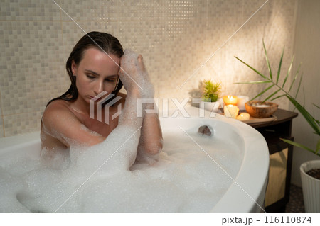 A woman relaxes in a bubble bath surrounded by candles and plants. The atmosphere of psychological problems experienced by a woman A woman relaxes in a bubble bath surrounded by candles and plants. The atmosphere of psychological problems experienced by a woman 116110874