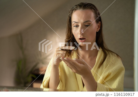 A woman in a bathroom, after taking a shower, ran her fingers through her wet hair and notices a concerning amount of hair falling out. 116110917