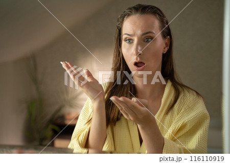 A woman in a bathroom, after taking a shower, ran her fingers through her wet hair and notices a concerning amount of hair falling out. 116110919