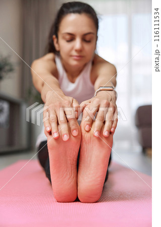 Sporty Caucasian woman worm up by stretching her body on pink exercise mat at home. focus on foot 116111534