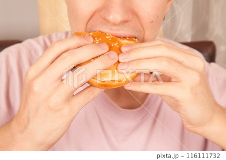 Caucasian young man eats half-eaten sesame fresh hamburger Caucasian young man eats half-eaten sesame fresh hamburger 116111732