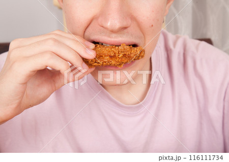 Caucasian man eating fried chicken wings, American fast food culture, cooked chicken pieces 116111734