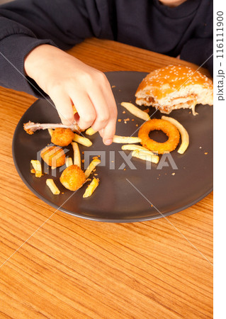 American fast food culture, half-eaten hamburger, potato chips, onion rings and chicken pieces in gray plate on wooden table 116111900