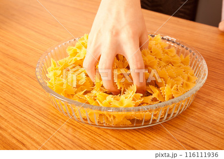 Uncooked raw healthy and pasta macaroni hand held by a Caucasian man, on wooden table in glass plate Uncooked raw healthy and pasta macaroni hand held by a Caucasian man, on wooden table in glass plate 116111936